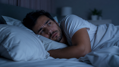 Homem acordado na cama durante a noite com expressão de insônia